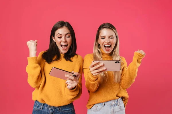 Две Счастливые Красивые Девушки Празднуют Успех Используя Мобильные Телефоны Изолированы — стоковое фото