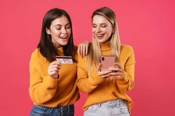 ピンクの壁の背景に隔離された携帯電話とクレジットカードでオンラインショッピング二人の幸せな若いガールフレンド — ストック写真