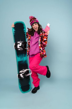 Güzel heyecanlı sporcu kadın mavi duvarın üzerinde izole edilmiş pasaport ve snowboard ile poz veriyor.