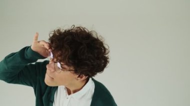 Gözlük takan genç bir adamın kırpılmış görüntüsü stüdyodaki gri duvarın üzerinde tek başına duran birini arıyor.