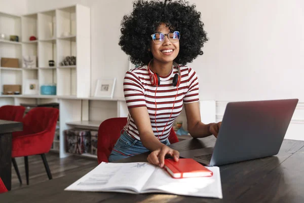 坐在室内餐桌旁 拿着笔记本电脑做作业的非洲裔美国女学生笑着 — 图库照片