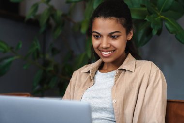 Kafede otururken dizüstü bilgisayarla çalışan gülümseyen Afrikalı Amerikalı kadın.