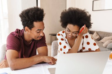 Güzel bir çift mutfakta dizüstü bilgisayarlarıyla oturuyor, birlikte çalışıyorlar.