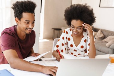 Güzel bir çift mutfakta dizüstü bilgisayarlarıyla oturuyor, birlikte çalışıyorlar.