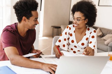 Güzel bir çift mutfakta dizüstü bilgisayarlarıyla oturuyor, birlikte çalışıyorlar.