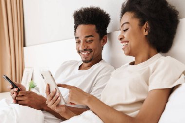 Koyu tenli adam ve karısı online iletişim için cep telefonu kullanıyorlar.