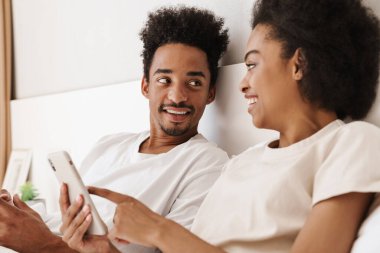 Koyu tenli adam ve karısı online iletişim için cep telefonu kullanıyorlar.