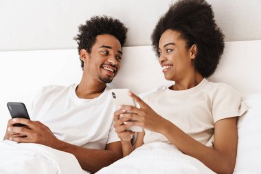 Koyu tenli adam ve karısı online iletişim için cep telefonu kullanıyorlar.