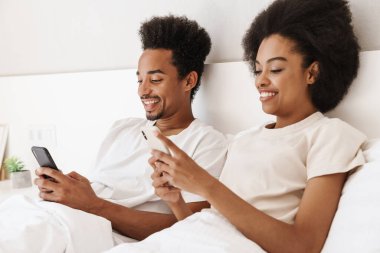 Koyu tenli adam ve karısı online iletişim için cep telefonu kullanıyorlar.