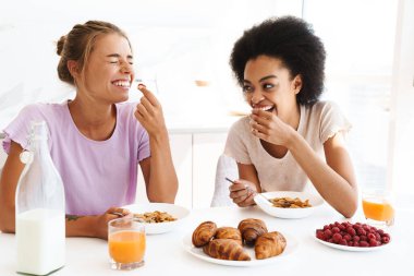 Güzel, neşeli, çok kültürlü kızlar birlikte kahvaltı ederken gülüyorlar.