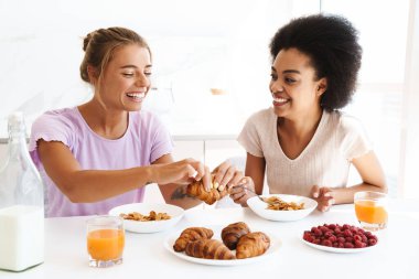 Mutfakta kahvaltı ederken gülümseyen neşeli, çok kültürlü kızlar.