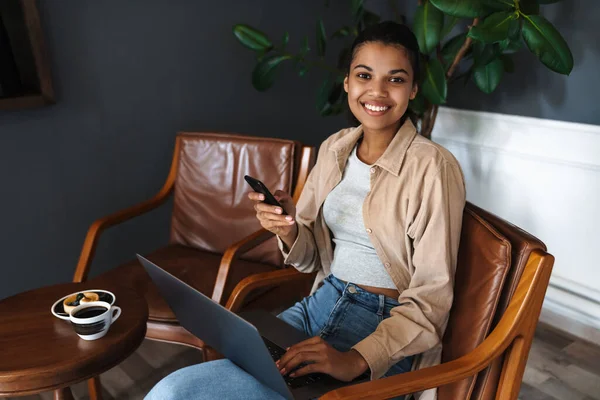 Усміхаючись Африканською Американською Жінкою Яка Працює Ноутбуком Мобільним Телефоном Сидячи — стокове фото
