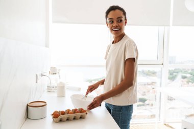 Evdeki mutfakta yemek pişiren Afrikalı genç bir kadının resmi.