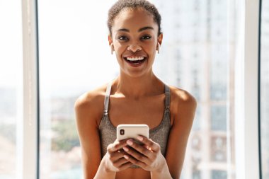 Genç, neşeli bir Afrikalı kadının cep telefonu kullanması ve kulaklıkla müzik dinlemesi.