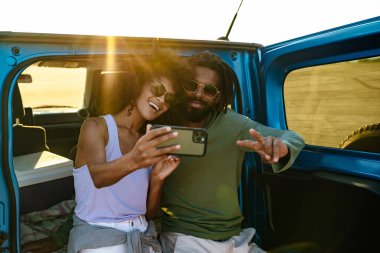 Genç çift arabada otururken akıllı telefon kullanarak selfie çekiyor.
