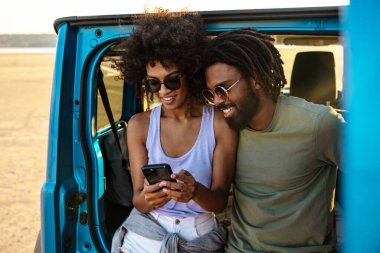 Güzel bir çift arabanın arkasında oturuyor ve akıllı telefonlar kullanıyorlar.