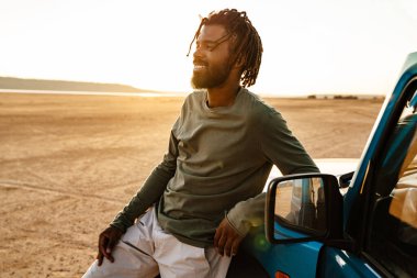 Çölde arabasıyla gezen ve gülümseyen Afro-Amerikalı bir adam.
