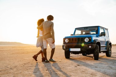Romantik Afrikalı Amerikalı bir çiftin çölde arabayla dolaşırken sarılıp yürümesi.