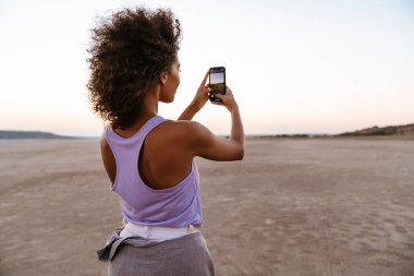 Çölde cep telefonuyla fotoğraf çeken güzel bir Afrikalı Amerikalı kadın.