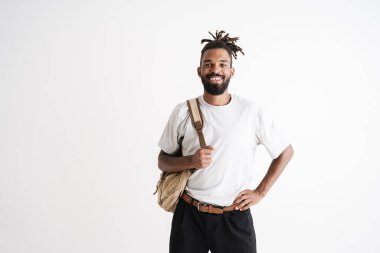 Beyaz arka planda izole edilmiş sırt çantasıyla poz verirken gülümseyen Afrikalı Amerikalı adamın fotoğrafı.