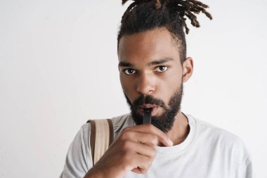 Beyaz arka planda izole edilmiş elektronik sigara içen traşsız Afro-Amerikan bir adamın fotoğrafı.