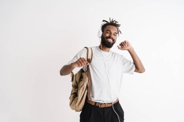 Beyaz arka planda izole edilmiş kulaklıklarla müzik dinleyen mutlu Afro-Amerikan adamın fotoğrafı.