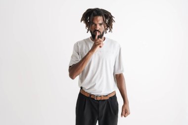 Beyaz arka planda izole edilmiş sessizlik işareti gösteren hoşnutsuz Afro-Amerikan bir adamın fotoğrafı.