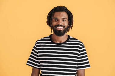 Sarı arka planda izole edilmiş kameraya bakıp gülümseyen neşeli Afrikalı Amerikalı adamın fotoğrafı.