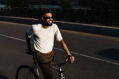 City Bridge 'de bisiklet sürerken gülümseyen mutlu Afrikalı Amerikalı adam.