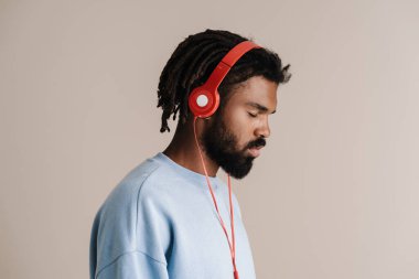 Beyaz arka planda izole edilmiş kulaklıklarla müzik dinleyen odaklanmış Afrikalı Amerikalı adam.
