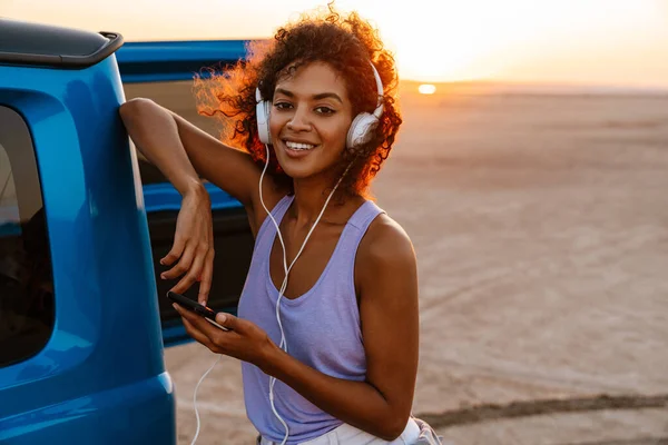 Εικόνα Μιας Χαρούμενης Αφροαμερικανής Που Χρησιμοποιεί Ακουστικά Και Κινητό Ενώ — Φωτογραφία Αρχείου
