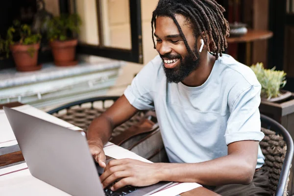 Veselý Africký Američan Sluchátkách Pracuje Notebookem Zatímco Sedí Kavárně Venku — Stock fotografie