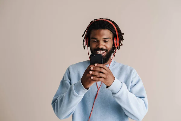 白い背景に隔離された携帯電話を使用してヘッドフォンで陽気なアフリカ系アメリカ人の男 — ストック写真