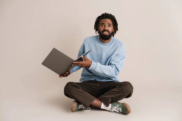 不快乐的非洲裔美国人坐在地板上 把笔记本电脑隔离在白色背景之外 — 图库照片