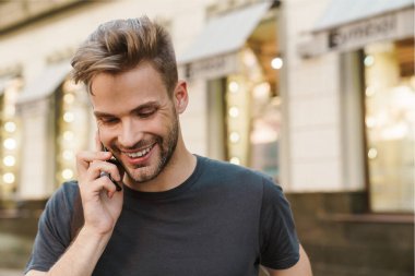 Gülümseyen çekici genç adam sokakta yürürken cep telefonuyla konuşuyor.