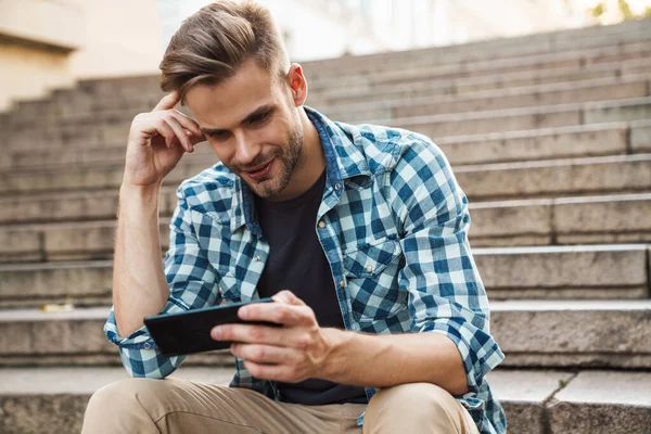Handsome Smiling Young Man Using Mobile Phone While Sitting Steps — Stock Photo, Image