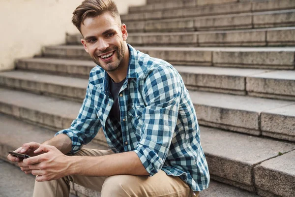 Handsome Smiling Young Man Using Mobile Phone While Sitting Steps — Stock Photo, Image