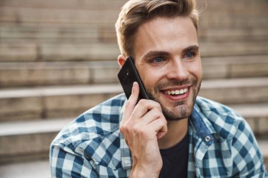 Genç adam dışarıda merdivenlerde otururken cep telefonuyla konuşuyor.
