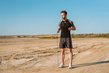 Yakışıklı genç sporcu sahilde ip atlayıp duruyor.