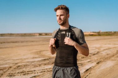 Yakışıklı genç sporcu sahilde ip atlayıp duruyor.