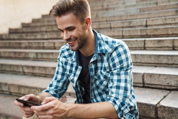 Handsome Smiling Young Man Using Mobile Phone While Sitting Steps — Stock Photo, Image