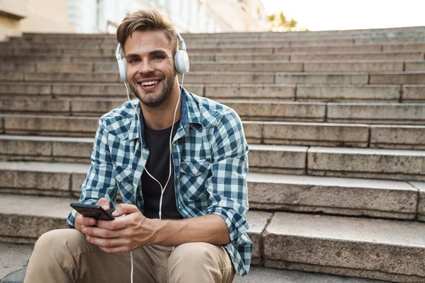 Bonito Homem Sentado Nas Escadas Com Fones Ouvido Telefone Celular — Fotografia de Stock