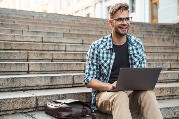 Junger Lächelnder Mann Sitzt Auf Stufen Und Arbeitet Draußen Laptop — Stockfoto