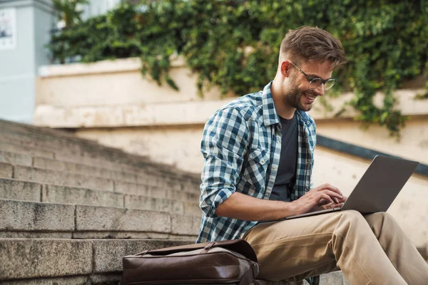 Junger Lächelnder Mann Sitzt Auf Stufen Und Arbeitet Draußen Laptop — Stockfoto