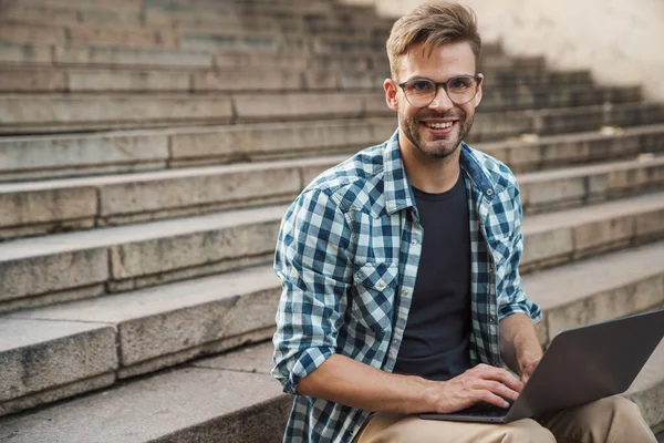 Joven Hombre Sonriente Sentado Los Escalones Trabajando Portátil Aire Libre — Foto de Stock