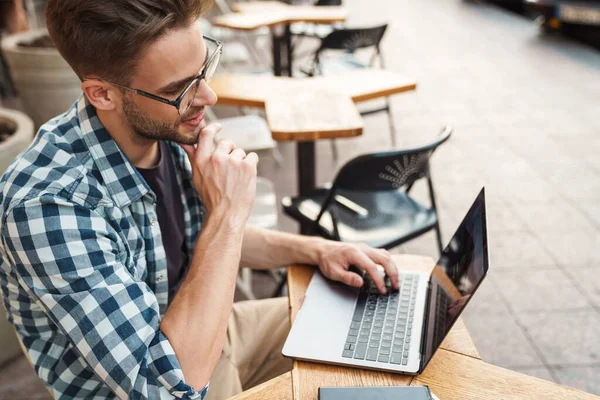 Szczęśliwy Młody Człowiek Pracujący Laptopie Siedząc Kawiarni Chodnikowej — Zdjęcie stockowe