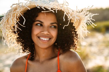 Sahilde poz veren mutlu, pozitif, genç bir Afrikalı kadın.