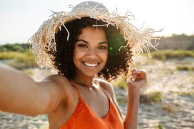 Gülümseyen Afrikalı bir kadın sahilde selfie çekiyor.