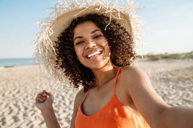 Güzel, mutlu, Afrikalı bir kadının dışarıda sahilde selfie çekerken görüntüsü.