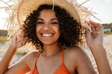 Sahilde yürüyen güzel, gülümseyen bir Afrikalı kadın.